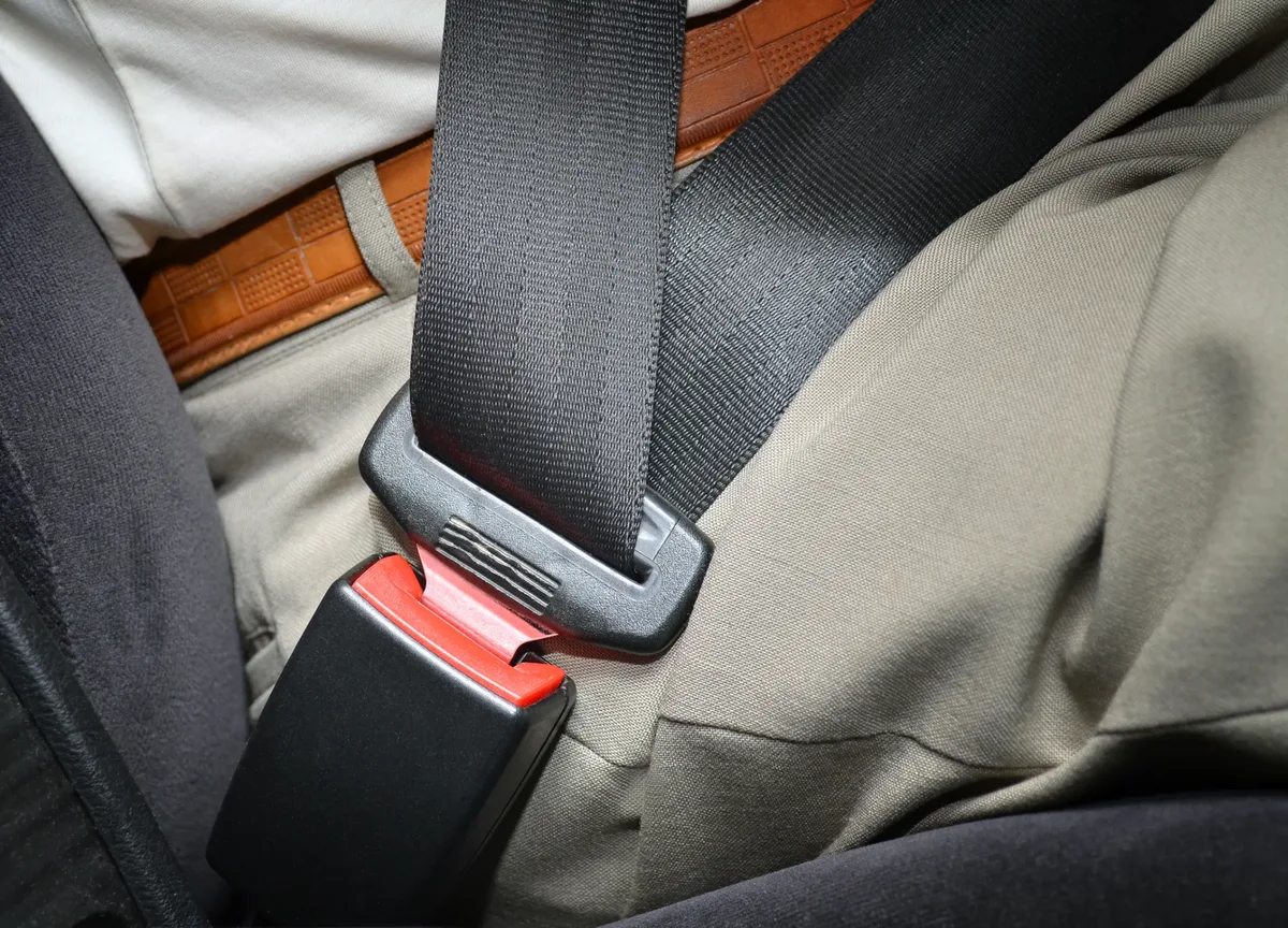 Lap section of a fastened seat belt lying across a seated occupant beside the buckle