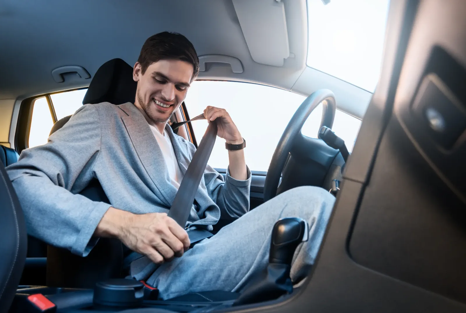 Occupant seated in a passenger car drawing the seat belt webbing across the body towards the buckle