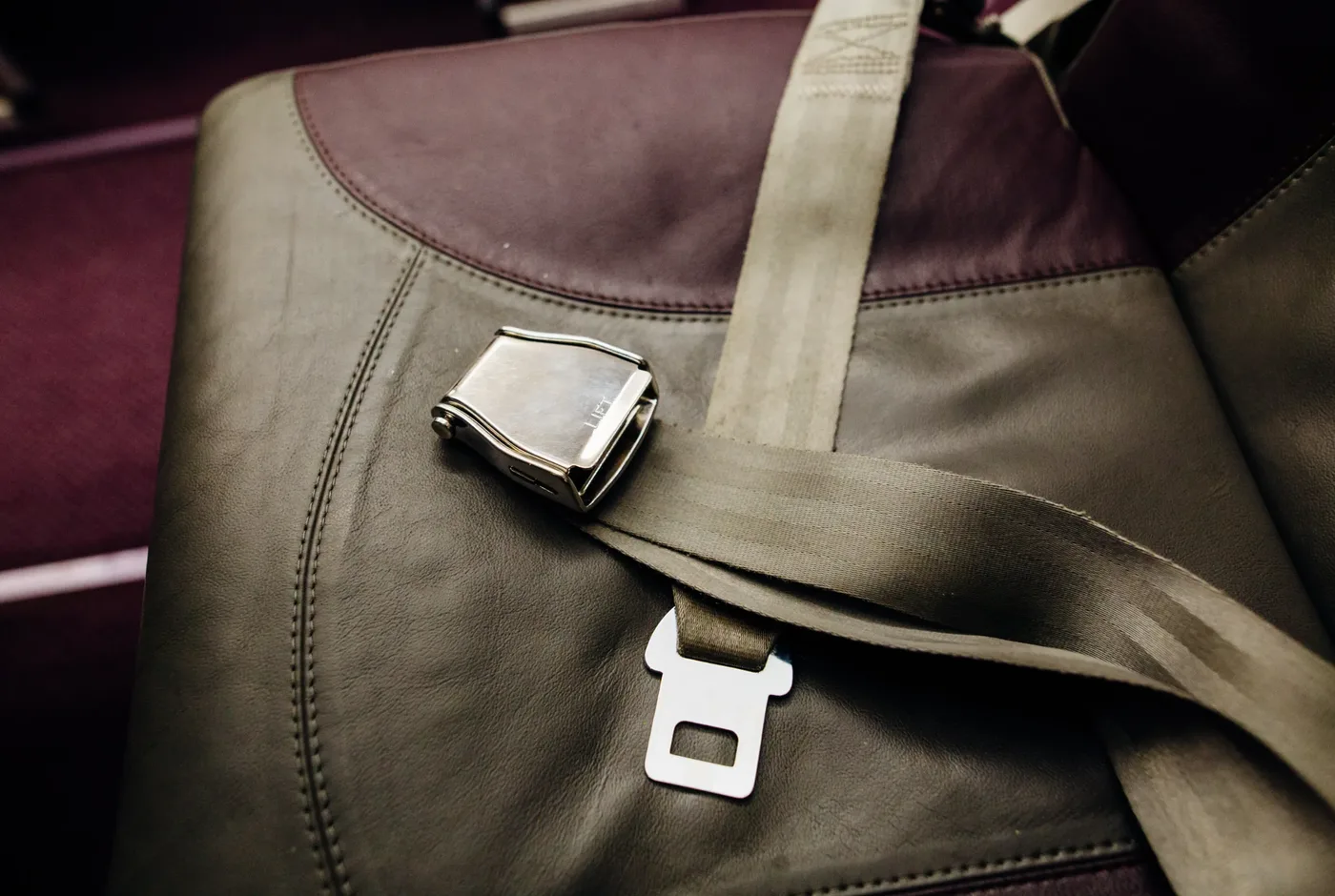 Lift-latch style restraint buckle and webbing fitted across an upholstered transport seat