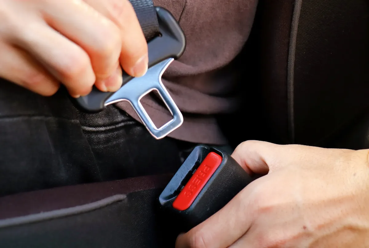 Hands drawing seat belt webbing out and guiding the tongue plate towards the buckle