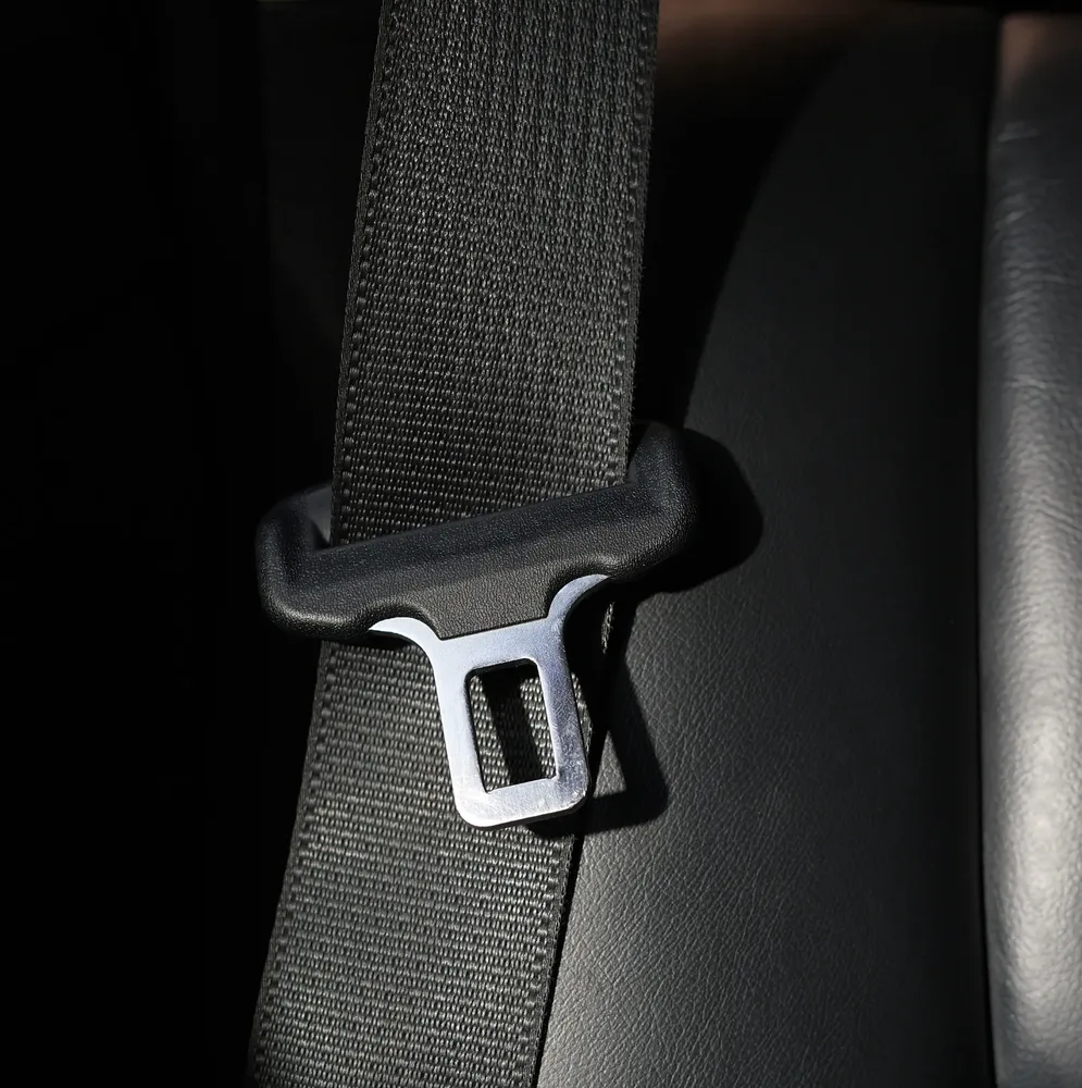 Close view of seat belt webbing and a polished tongue plate against a dark leather seat