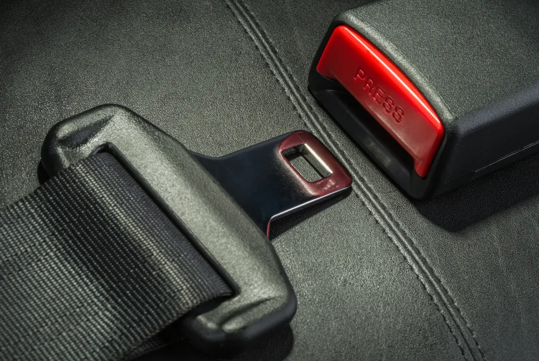 Complete seat belt assembly showing webbing, tongue plate and buckle housing on a dark vehicle seat