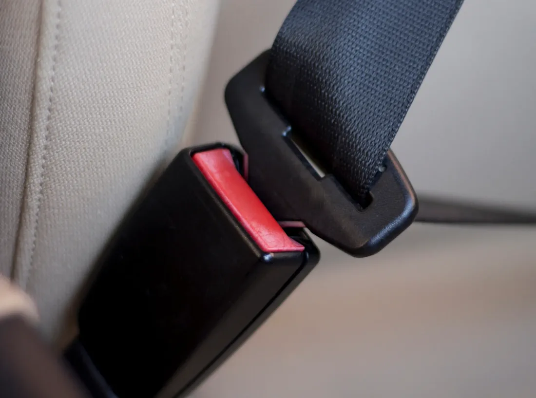 Close-up of a seat belt buckle with red press release button alongside the mating tongue plate