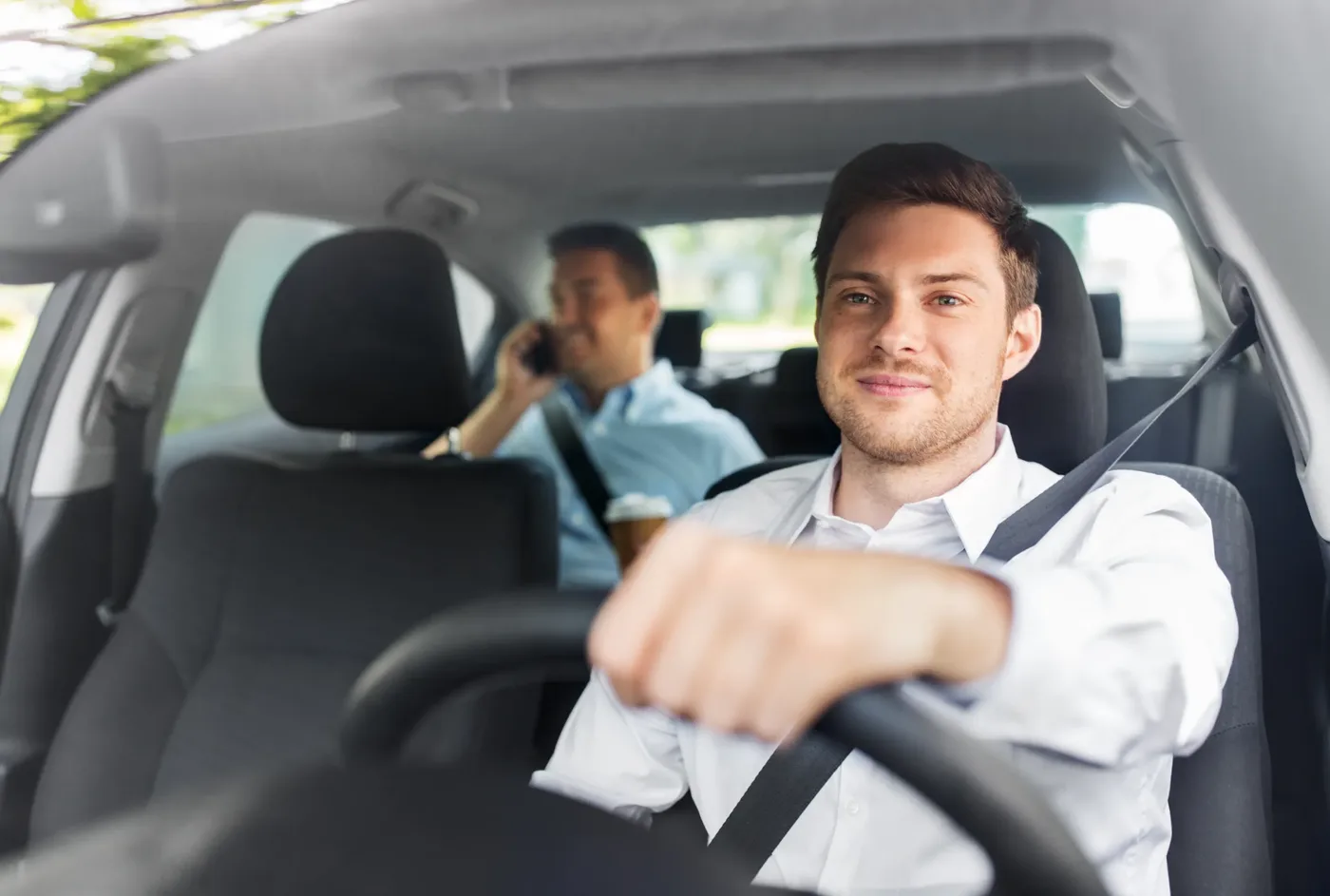Driver and front passenger seated in a car with three-point seat belts fastened across the shoulder