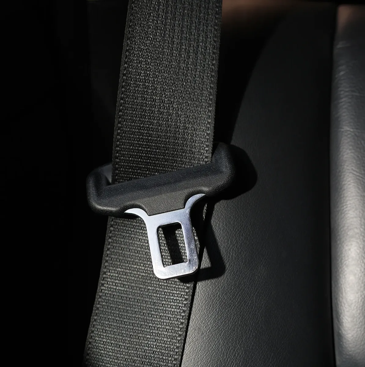 Close view of woven seat belt webbing and a metal tongue plate on a dark leather seat
